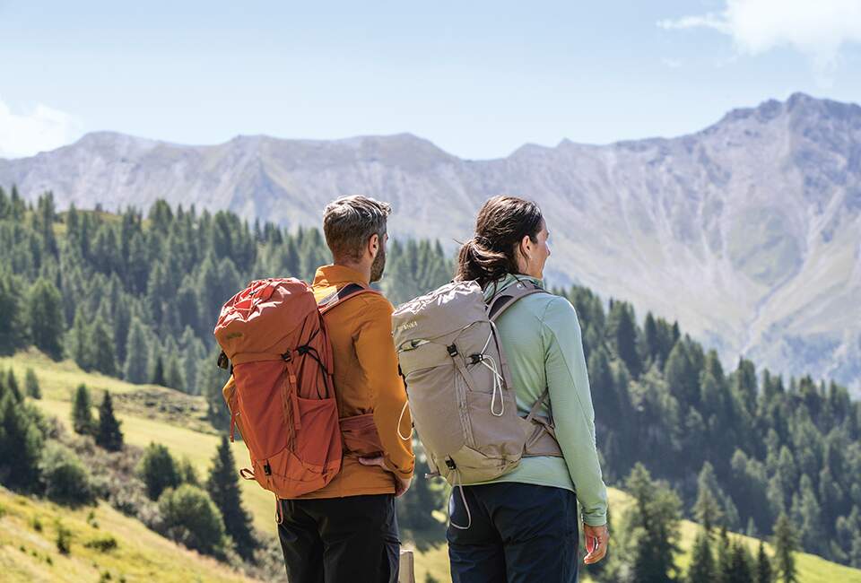 Ein Mann und eine Frau tragen Outdoorkleidung stehen auf einem Berg.
