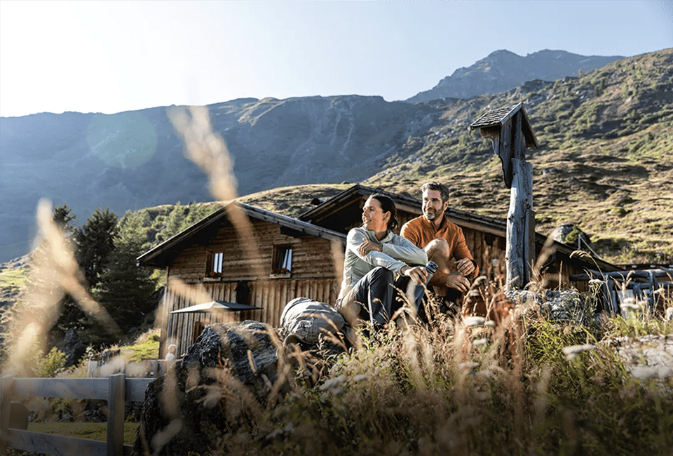Eine Frau und ein Mann sitzen vor einer Holzhütte in den Bergen.