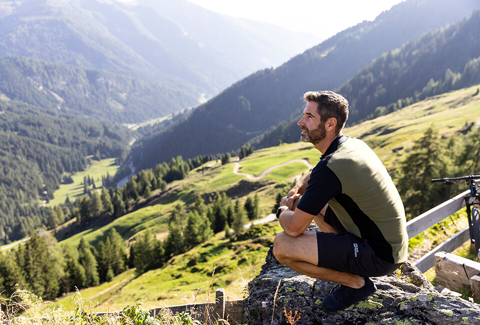 Ein Mann trägt Outdoorkleidung und sitzt auf einem Berg.